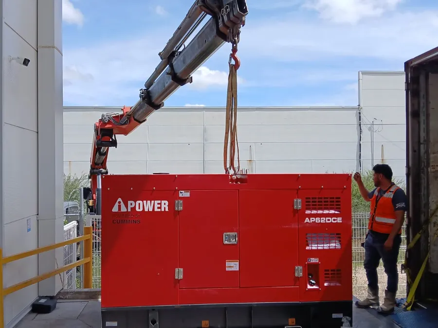 Planta de emergencia roja bajada con una grúa junto a una nave industrial