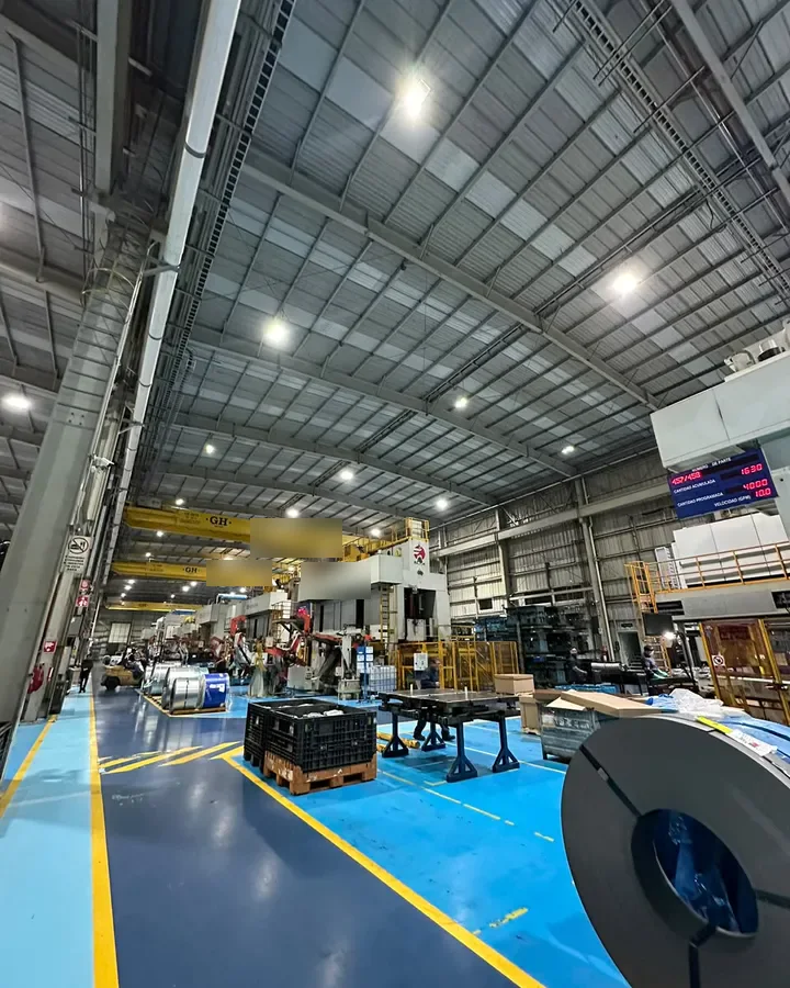 Interior de una nave industrial con campanas LED encendidas en el techo y maquinaria al fondo